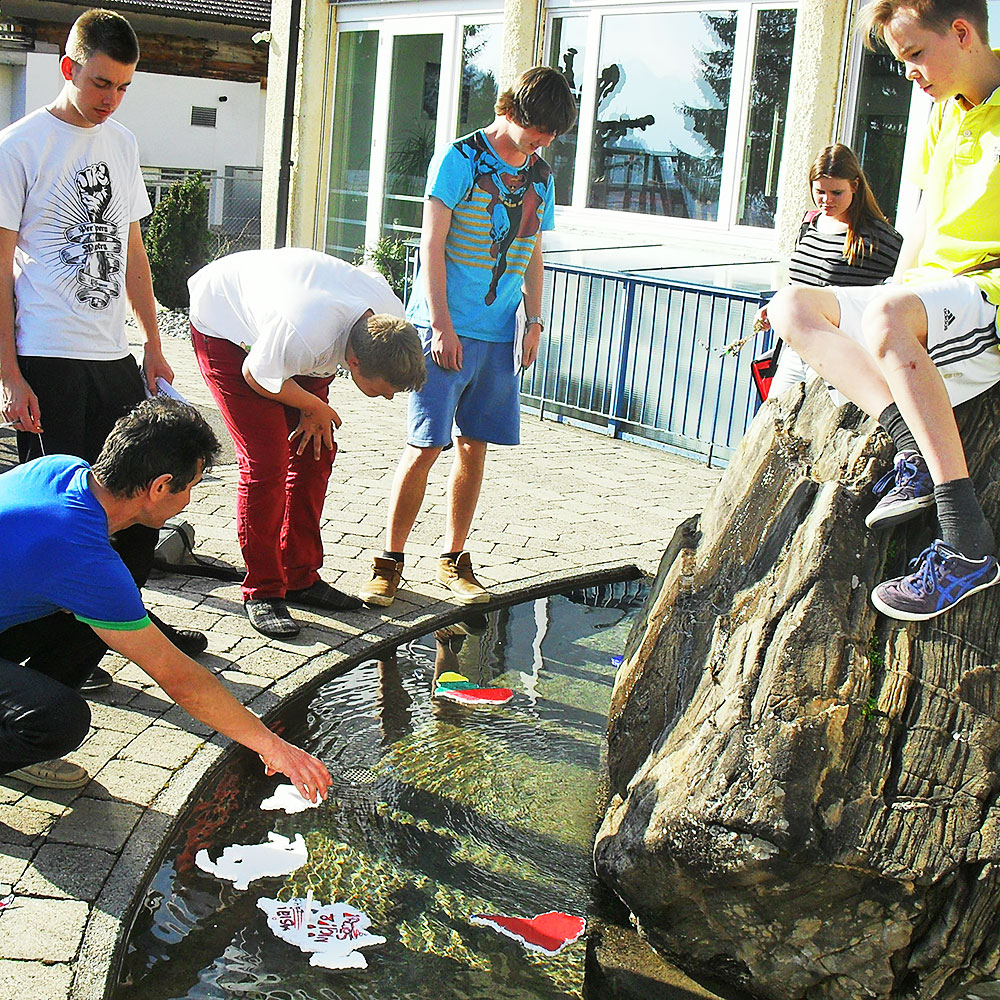 eine Klasse führt Wasserexperimente im Schulbrunnen durch